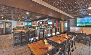Un ristorante con diversi tavoli e sedie, una zona bar con uno schermo televisivo e un'indicazione per il bagno.