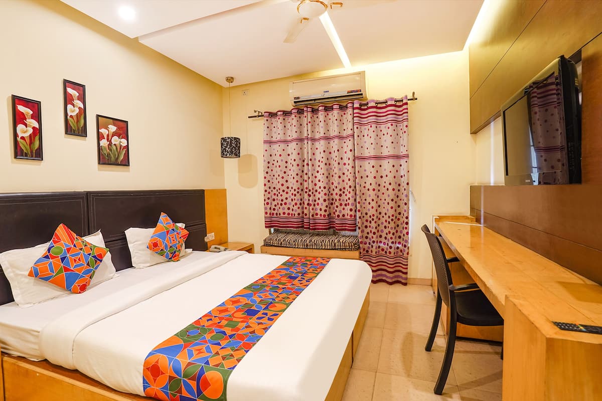 A hotel room with a bed, a desk, and a chair. There are three paintings on the wall.