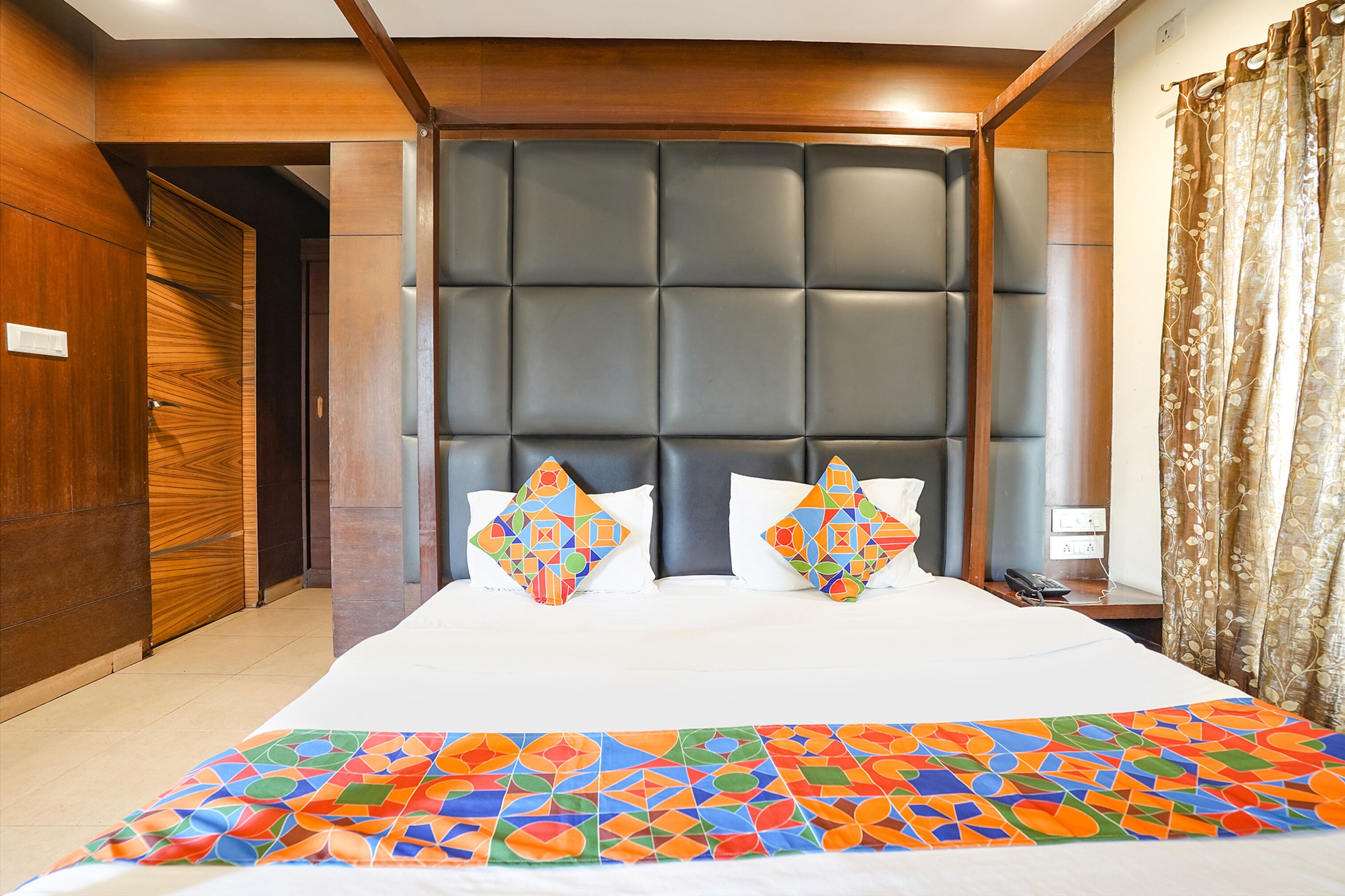 Une chambre d’hôtel avec un grand lit, une tête de lit en bois et une couvre-lit aux couleurs vives.