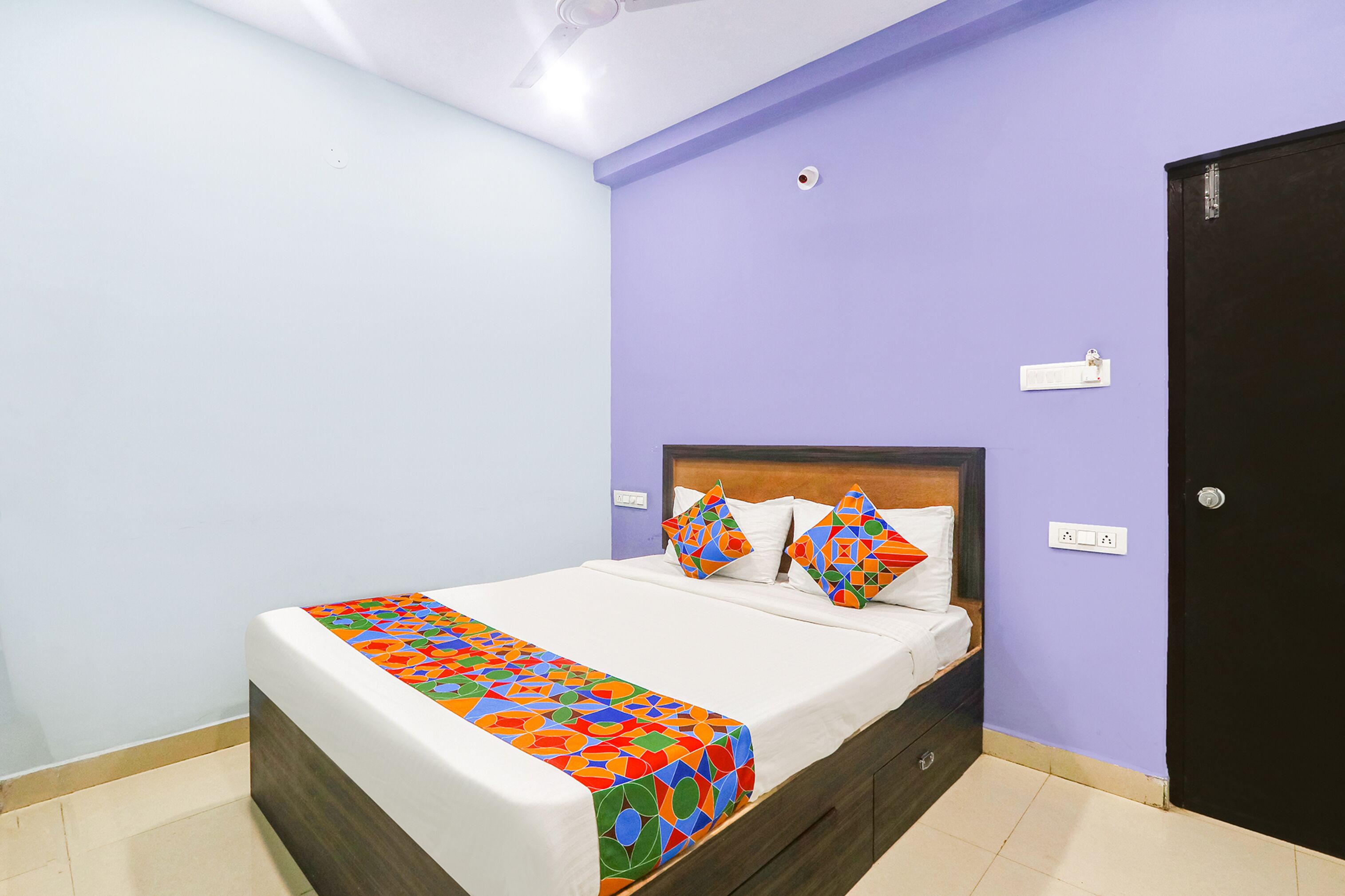A neatly made bed with a colorful bedspread, a wooden headboard, and two pillows.