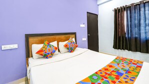 A hotel room with a bed, two colorful pillows, a patterned rug, a dark curtain, and a door. - Fabexpress Night Eye (Hyderabad)