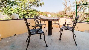 Un patio con dos sillas de metal ornamentadas y una pequeña mesa, rodeado por un muro bajo y árboles.
