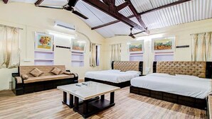 Una habitación de hotel con sofá, dos camas individuales, una mesa de centro y obras de arte en las paredes.