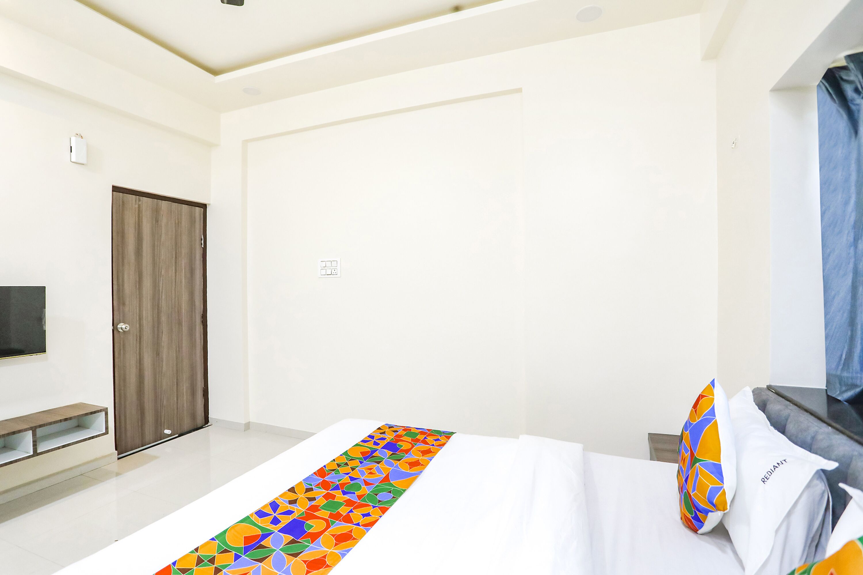 A hotel room with a bed, a TV, a wardrobe, and a bench.