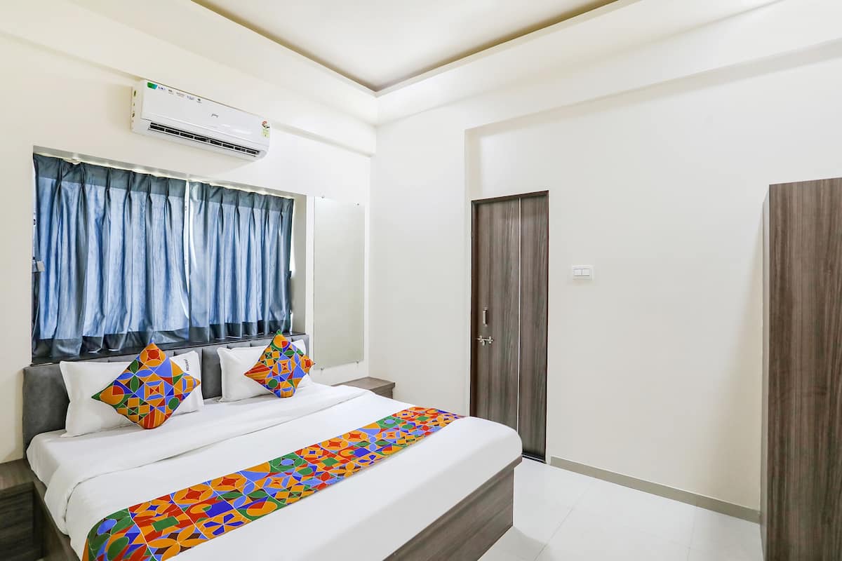 Una habitación de hotel con cama, ventana con cortinas, aire acondicionado y armario.