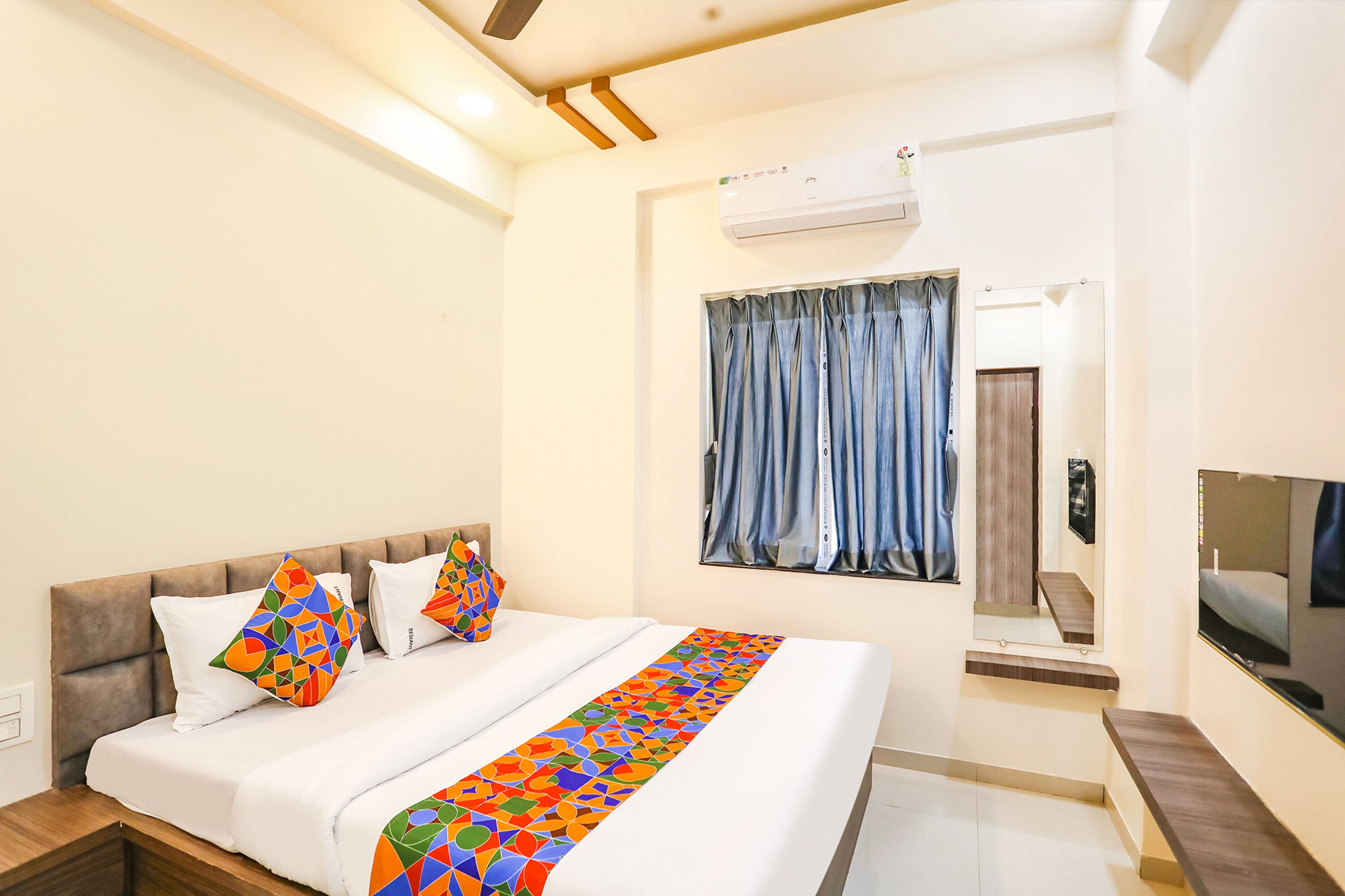 A hotel room with a bed, a TV, a window with curtains, and an air conditioning unit.