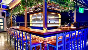 A bar area with a wooden counter, blue chairs, and shelves of bottles. - FabHotel Prime BT Wellness With Pool (Morjim)