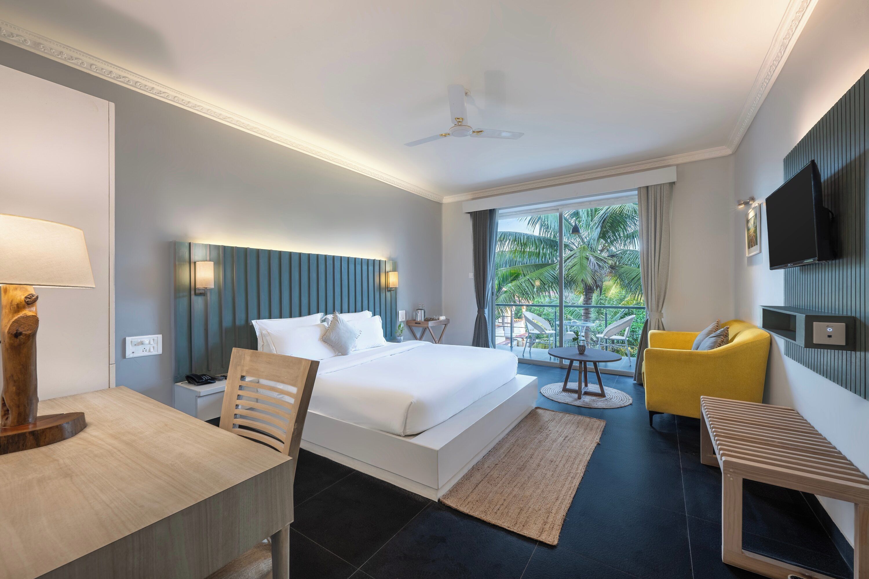 A modern hotel room with a large bed, a desk, a yellow armchair, and a television.