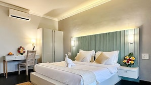 A hotel room with a large bed, a desk, a chair, and a nightstand with a lamp. - FabHotel Prime BT Wellness With Pool (Morjim)