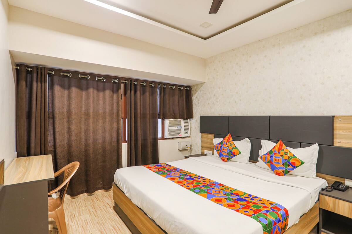 A hotel room with a bed, a desk, a chair, and a window with curtains.
