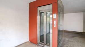 An elevator with a glass door, a red frame, and a control panel on the wall. - Fabhotel All Near (Raipur)