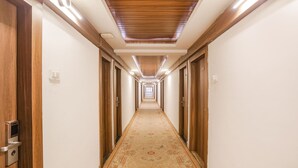 A hotel corridor with wooden doors, a patterned carpet, and a ceiling with recessed lighting. - Fabhotel All Near (Raipur)