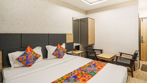 A hotel room with a large bed, two chairs, a small table, and a wardrobe. - Fabhotel All Near (Raipur)