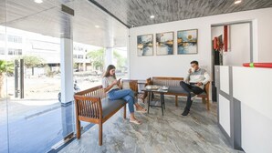 Un espace de détente intérieur moderne, doté de bancs en bois et d’un sol en marbre, agrémenté d’œuvres d’art sur les murs et d’une entrée en verre donnant sur l’extérieur.