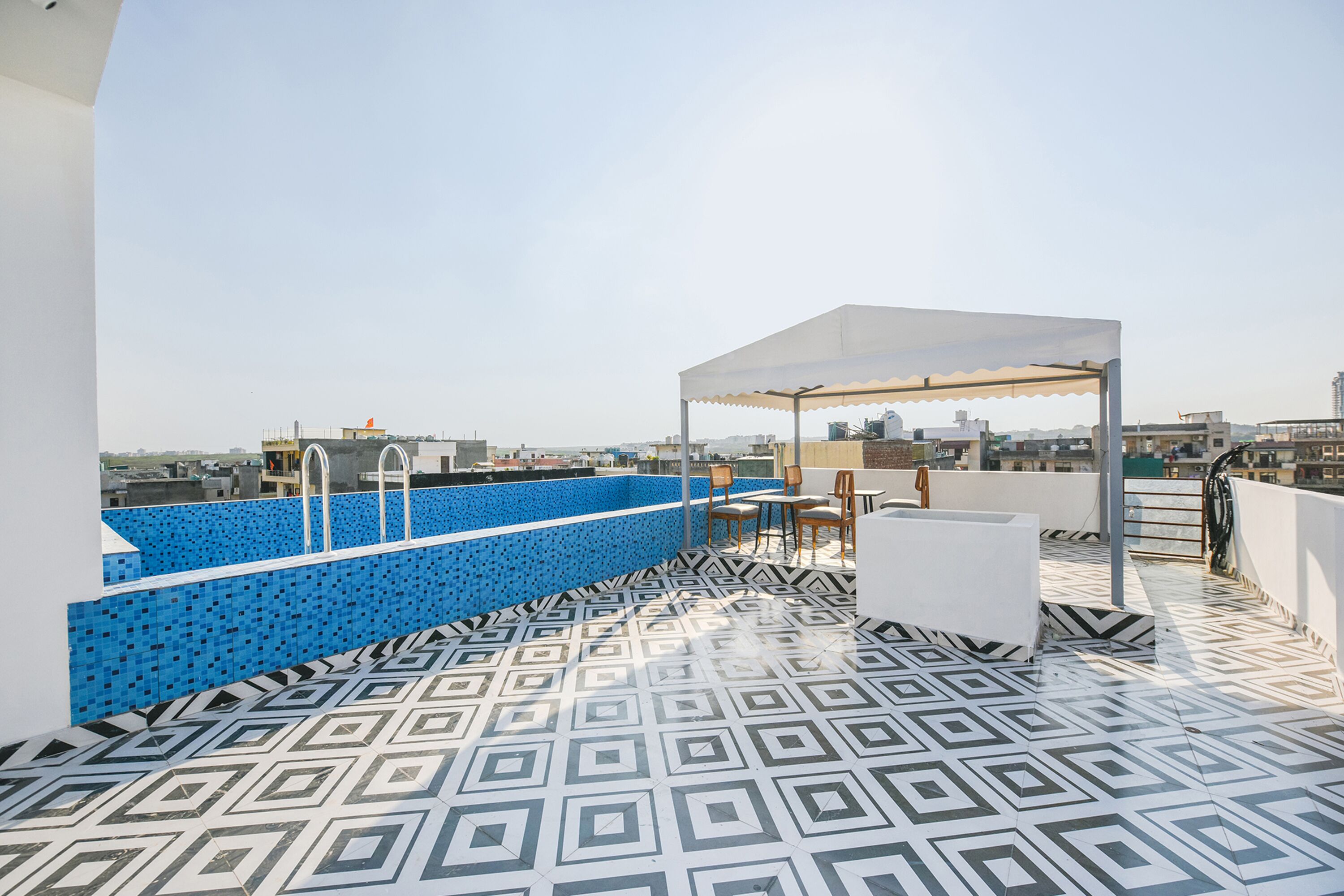 A rooftop pool area with a geometric patterned floor, a blue pool, and a covered seating area.