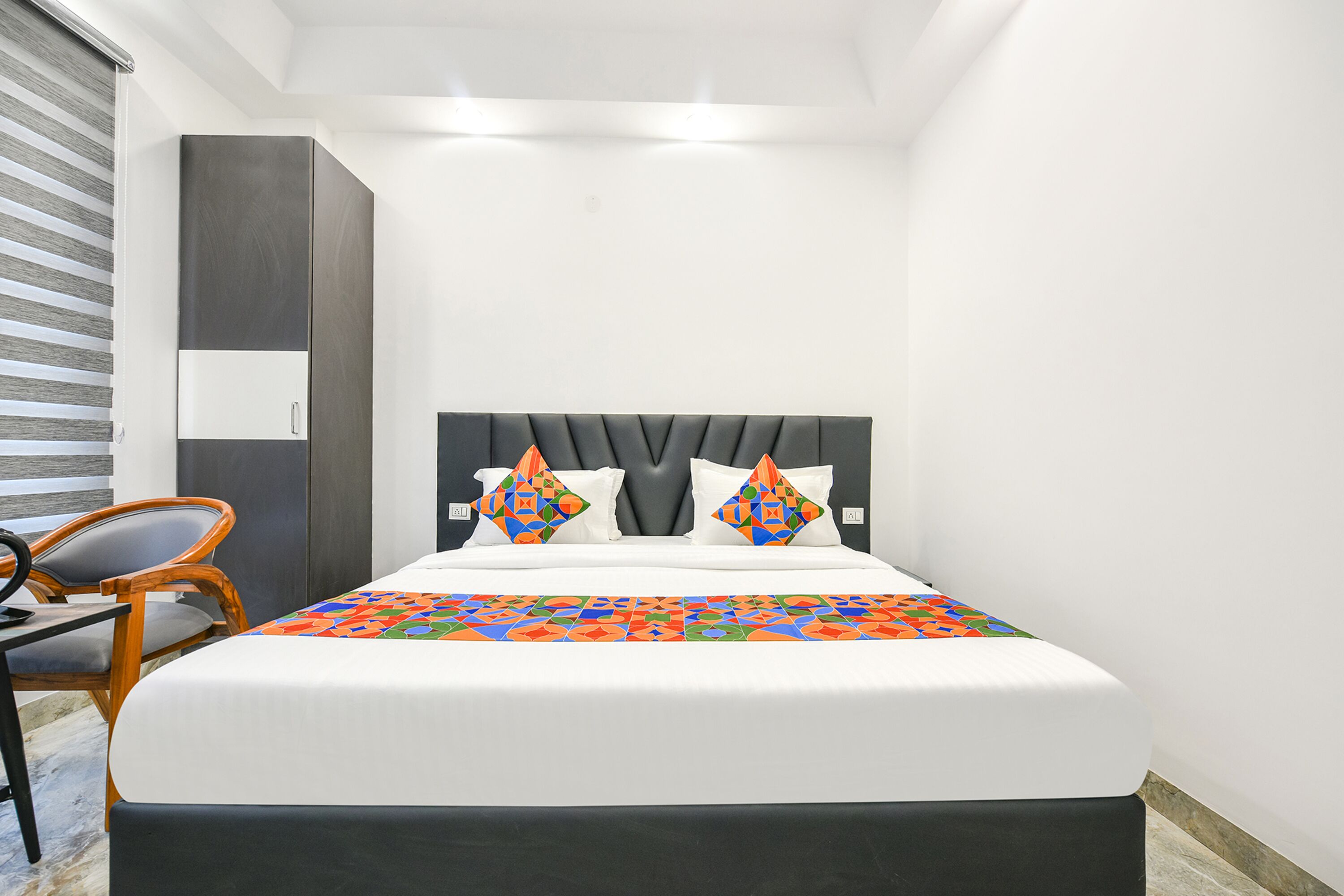 A modern hotel room with a large bed, a wooden chair, and a wardrobe.