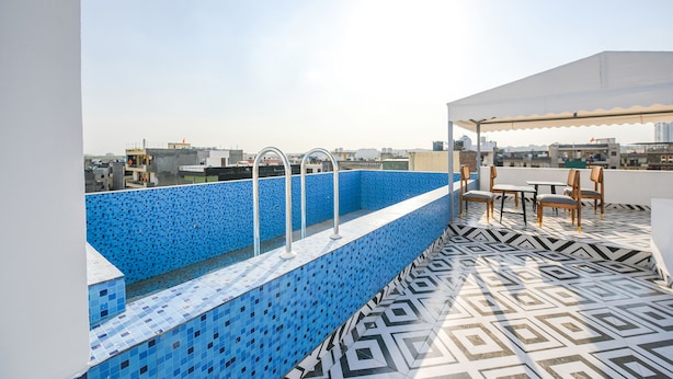 Une piscine sur le toit, avec des carreaux bleus et un sol à motifs géométriques, entourée de mobilier d’extérieur.