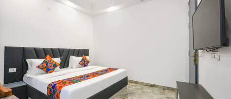 A bedroom with a bed, a flat-screen TV, a ceiling fan, and a stone floor.