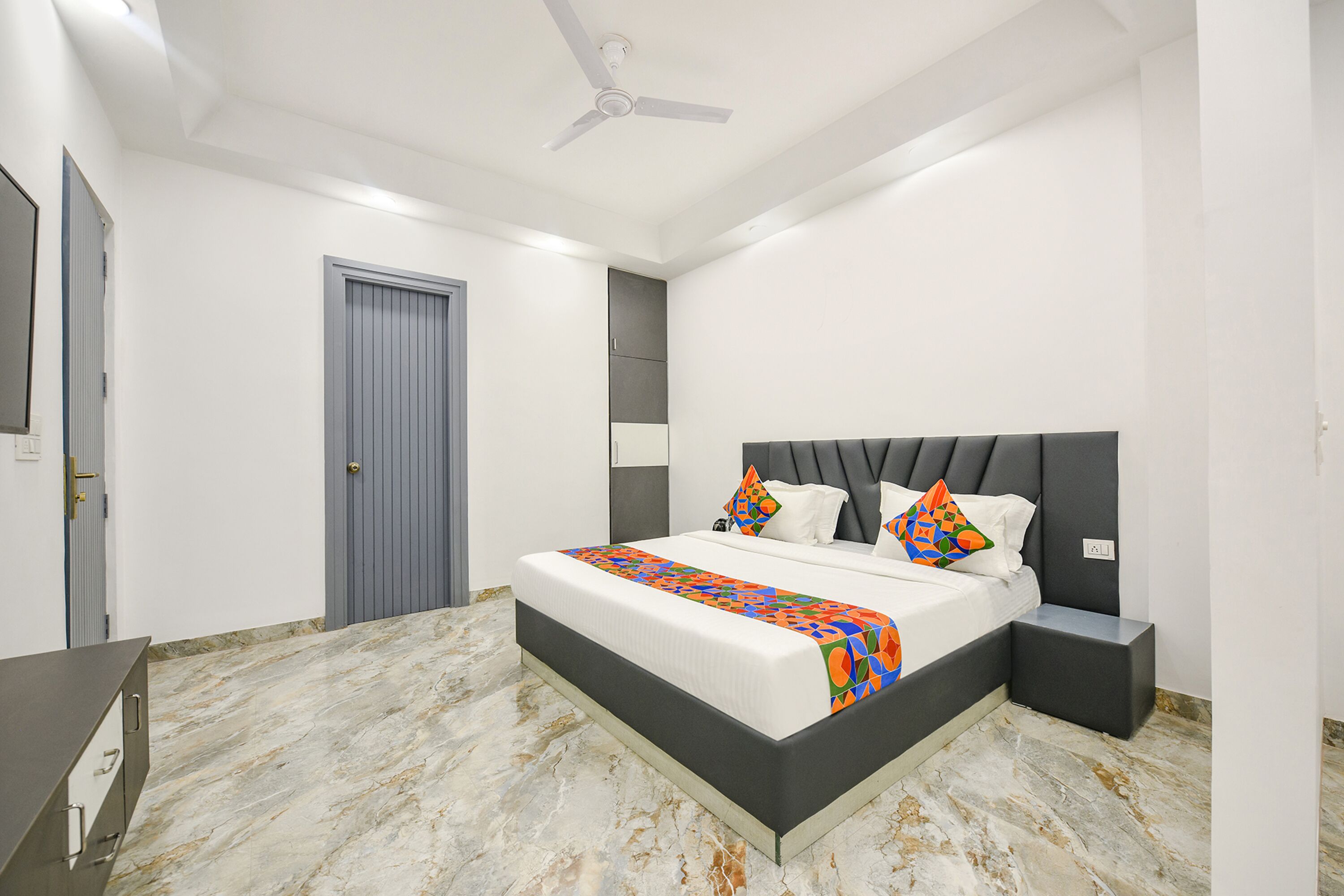 Une chambre à coucher comprenant un lit, des tables de chevet, un bureau et un ventilateur de plafond.