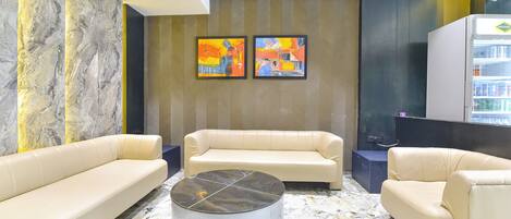 Um lobby moderno com piso de mármore, dois sofás, uma mesa de centro e quadros abstratos nas paredes.