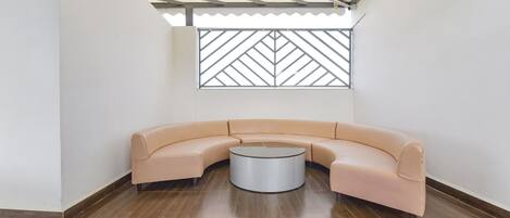 A modern interior with a curved beige sofa, a round coffee table, and a geometric patterned window.