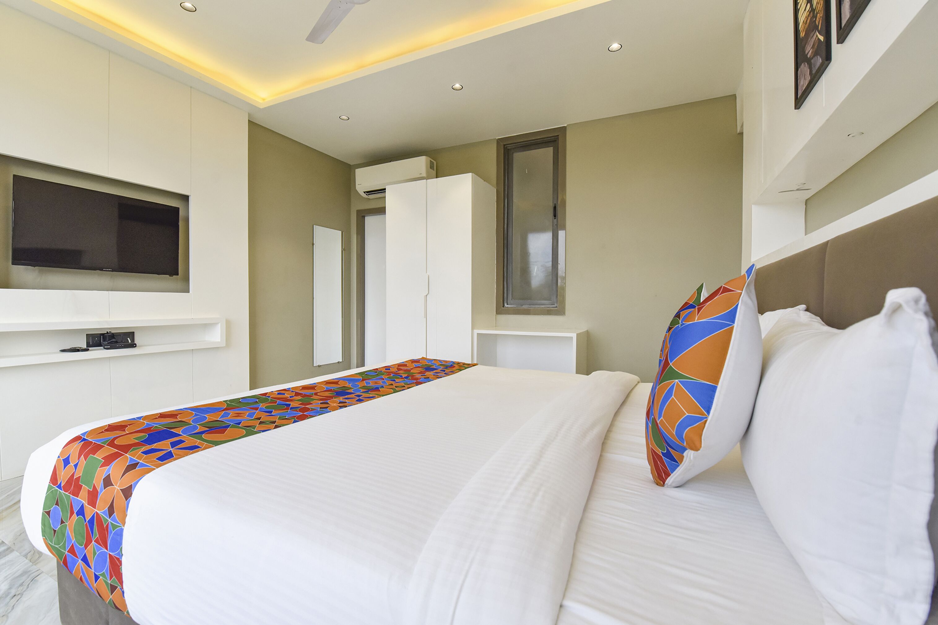 A hotel room with a bed, a television mounted on the wall, a window, and a ceiling fan.