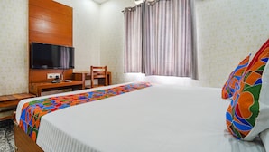 A hotel room with a bed, a desk, a chair, a television, and a window with curtains. - Fabexpress Elegant Residency (Chennai)