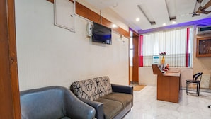 A living room with a sofa, a television mounted on the wall, a wooden desk, and a chair. - Fabexpress Elegant Residency (Chennai)