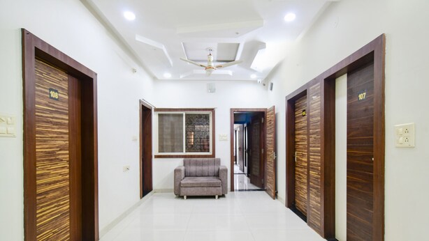 A hallway with two doors labeled 108 and 107, a grey sofa, and a ceiling fan. - Fabexpress Olive Inn (Ujjain)