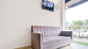 A grey sofa in a room with a tiled floor and a TV mounted on the wall. - Fabexpress Olive Inn (Ujjain)
