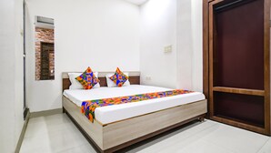A bedroom with a bed, a wooden door, and a small window with a brick pattern. - Fabexpress Olive Inn (Ujjain)