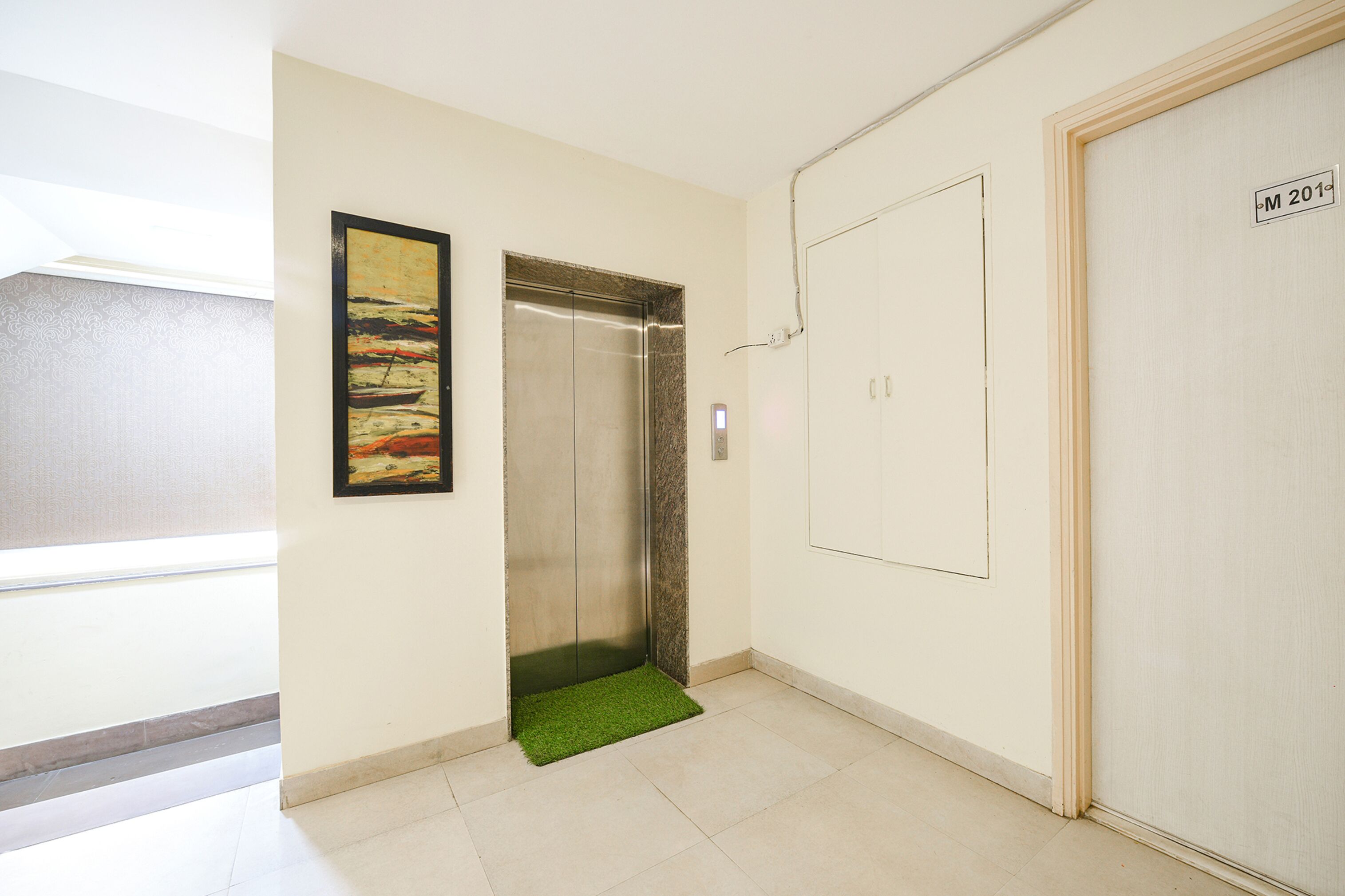 A hallway with an elevator, a door marked "M 201", and a framed painting on the wall.