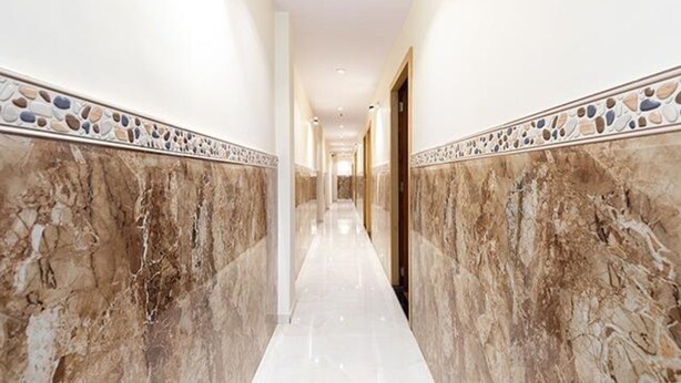 A corridor with marble walls and a polished floor, leading to a door. - Fabexpress Green House (Mumbai)