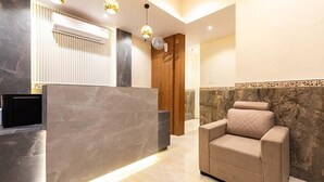 A reception area with a marble reception desk, a beige armchair, and a wooden door. - Fabexpress Green House (Mumbai)