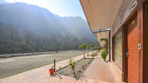 A hotel with a wooden exterior, a paved walkway, and a view of a river and mountains.