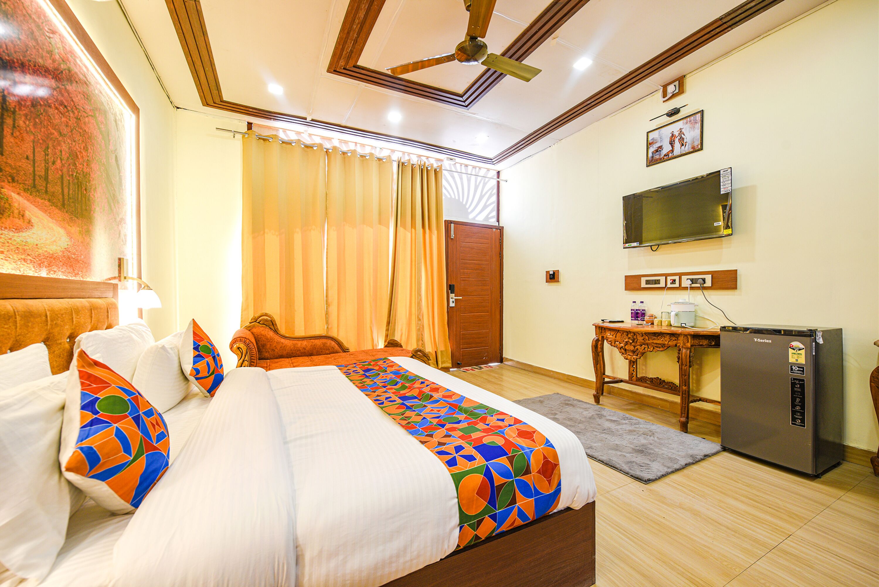 A hotel room with a bed, a desk, a refrigerator, a television, and a door.