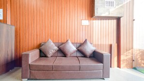 A brown leather sofa with three cushions against a wooden wall. - Fabhotel Sage Residency (Indore)