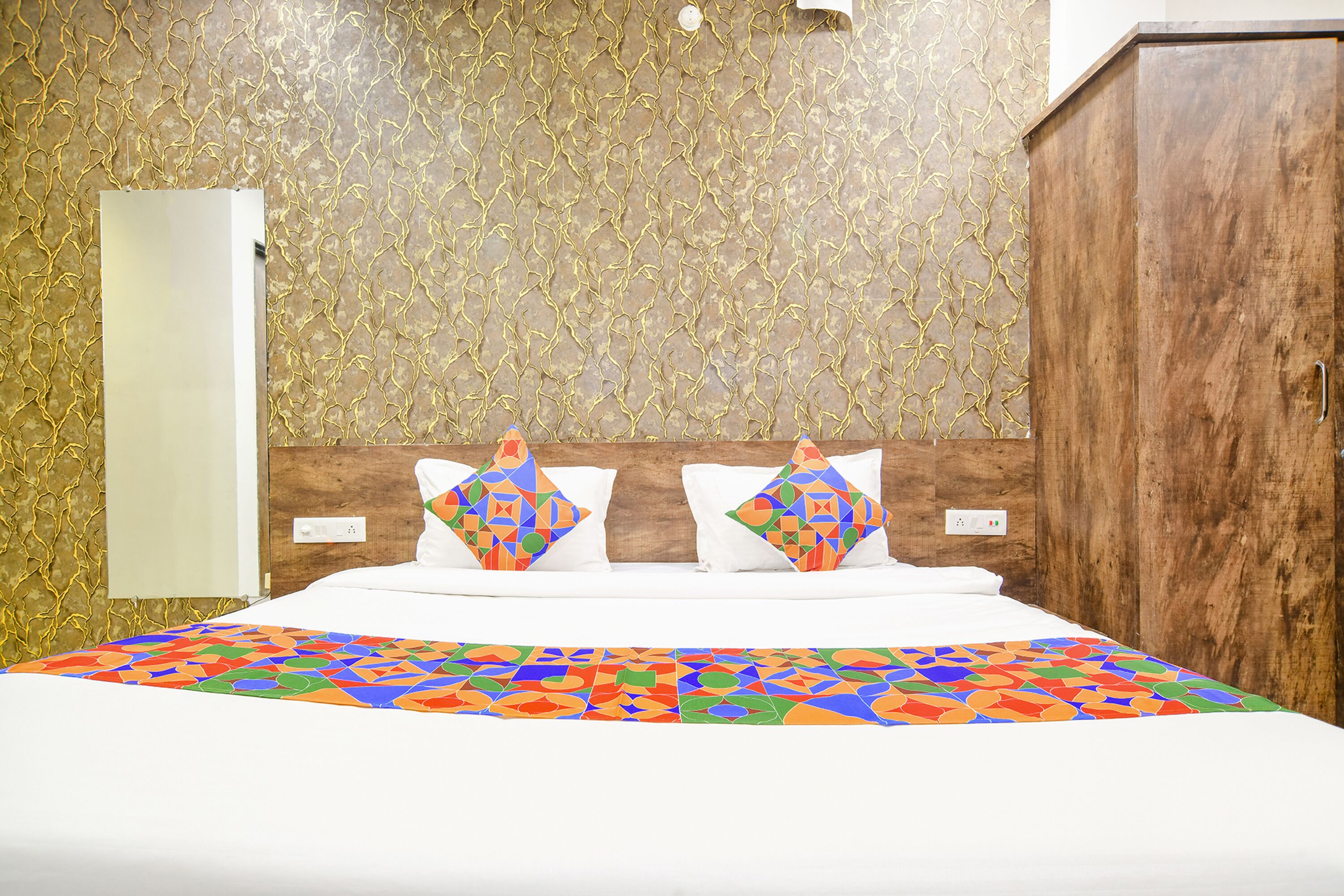 Une chambre d’hôtel avec un lit, deux oreillers, une armoire en bois et un mur décoré d’un motif.