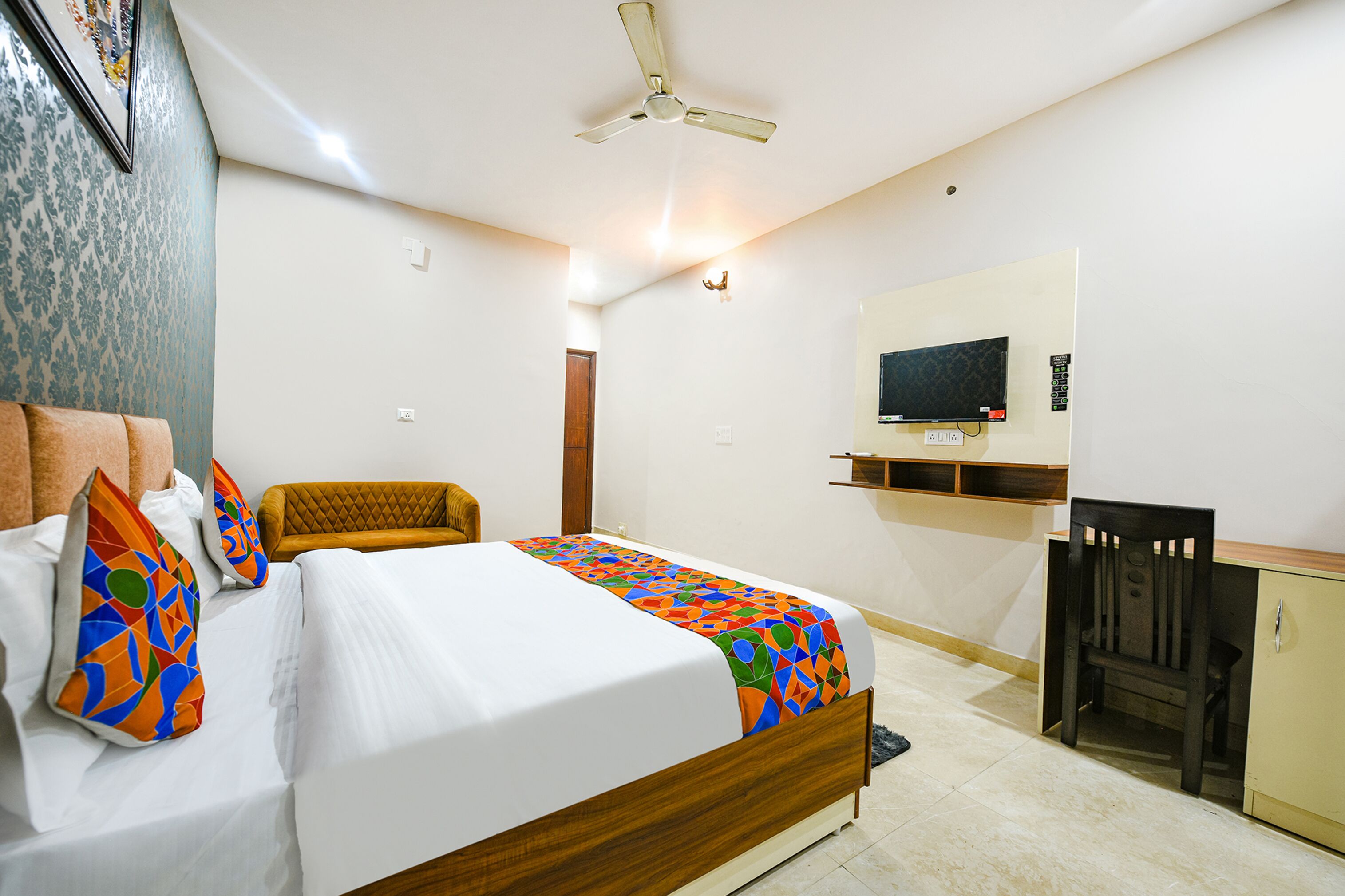 Habitación de hotel con cama, escritorio, silla, televisor y ventilador de techo.