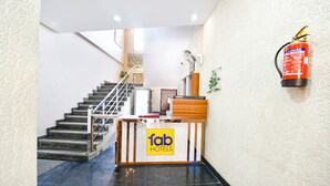 Een hotel receptie met een trap, een receptiebalie en een brandblusser aan de muur.