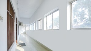 Un pasillo largo y estrecho con paredes blancas y ventanas amplias a un lado.