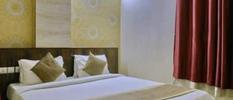 Una habitación de hotel con una cama grande, cabecera con panel decorativo, ventana con cortinas y pared con diseño estampado.