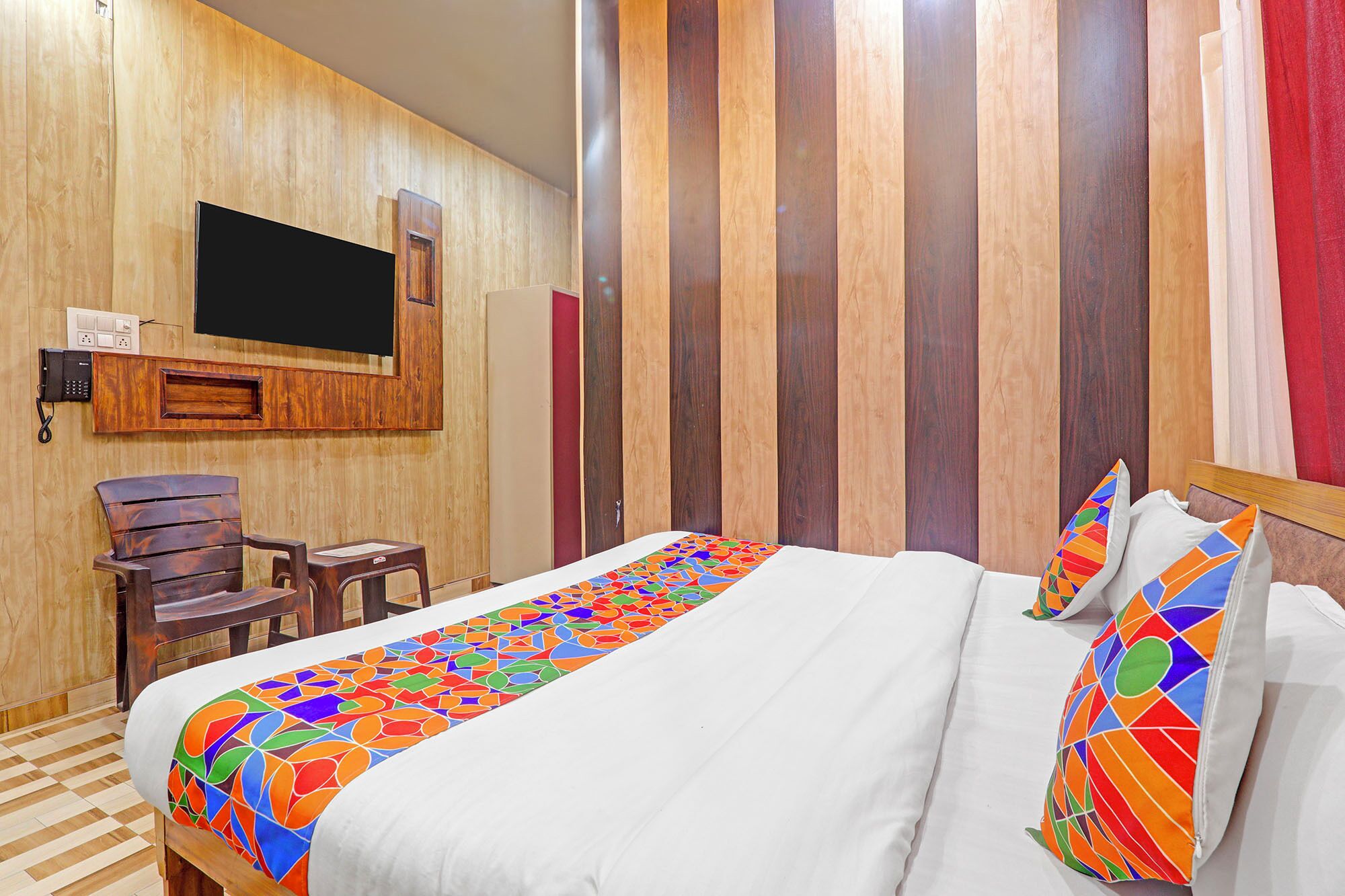 A hotel room with a bed, a desk, a chair, a TV mounted on the wall, and a striped wall.