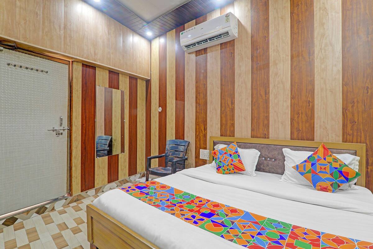 A hotel room with a bed, a chair, a mirror, and an air conditioning unit.