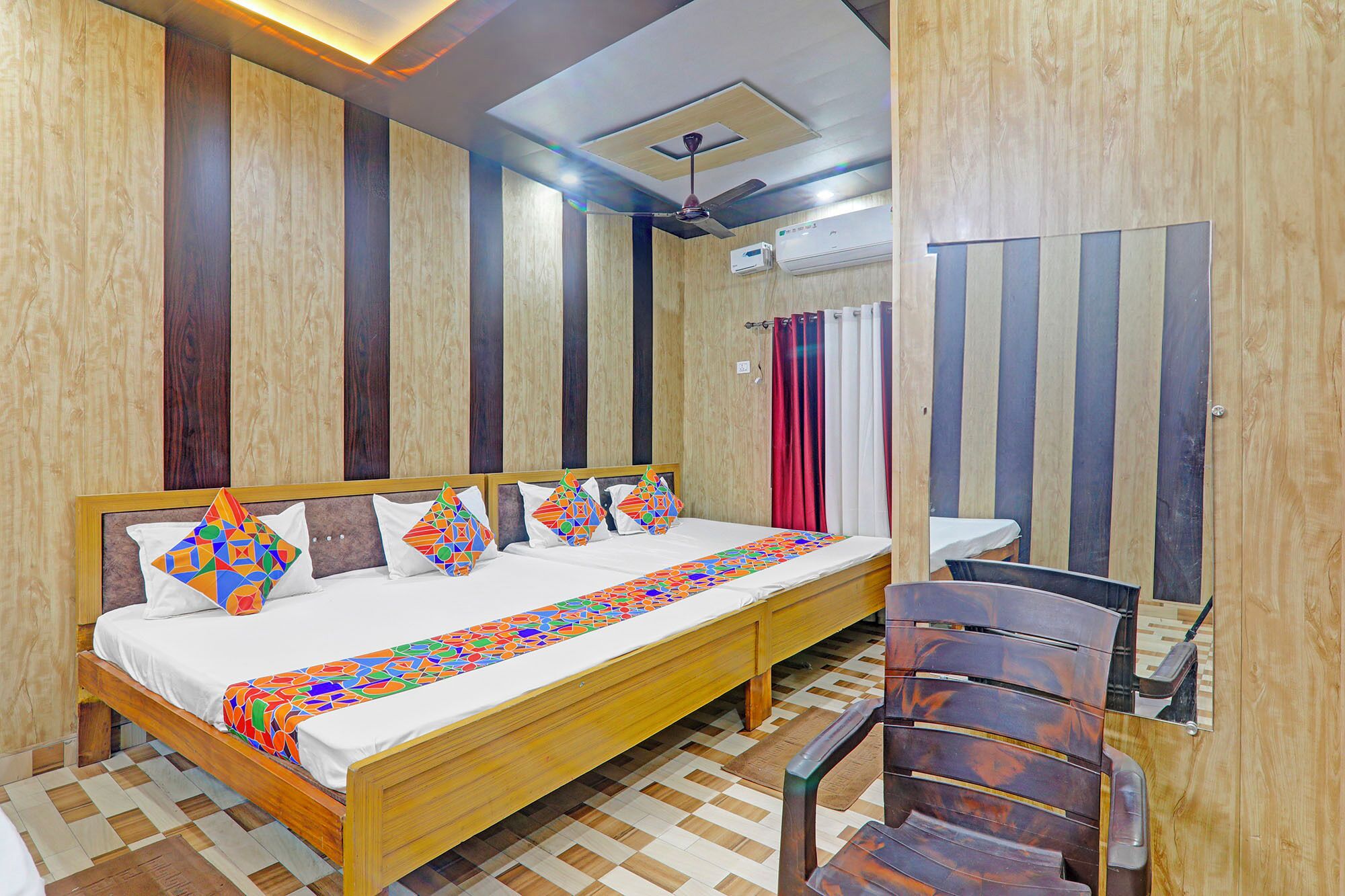 A hotel room with a wooden bed, a ceiling fan, an air conditioning unit, and a checkered floor.