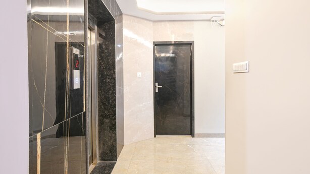 A modern hallway with a marble floor, a glass elevator, and a black door with a digital display.
