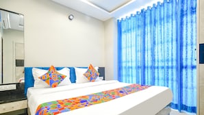 A hotel room with a large bed, a bathroom with a mirror, and blue curtains.