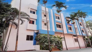 A multi-story building with a blue and white facade, palm trees, and a clear sky. - Via Paradise Stay Inn (Mawal)