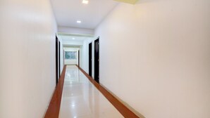 A long, narrow hallway with white walls and a shiny floor, leading to a door at the end. - Via Paradise Stay Inn (Mawal)