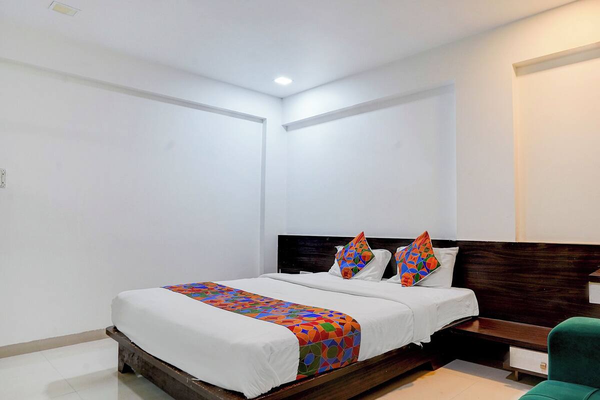 A bedroom with a wooden bed frame, white bedding, and colorful geometric pillows.